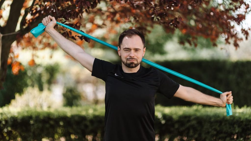 Adult man in black shirt exercises with a resistance band outside.